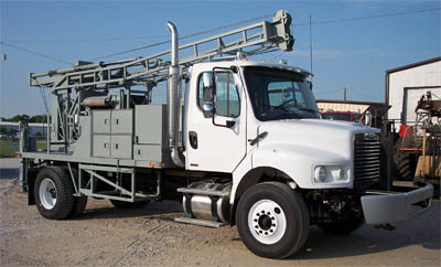 White Mobile B-57 drilling truck with tall drilling mast in equipment yard